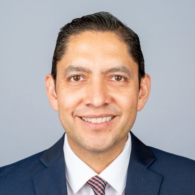 Alexander J. Gonzalez, licensed California real estate broker, smiling in a navy suit